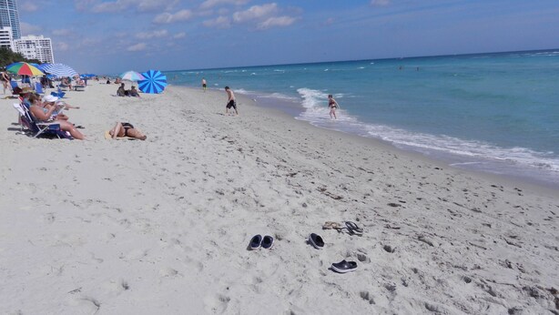 Une plage avec des empreintes de pas, quelques personnes et des parasols.