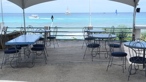 Una terrazza esterna con tavoli e sedie, affacciata sull'oceano con alcune barche a vela all'orizzonte.