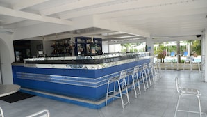 Angolo bar con bancone in piastrelle blu, sgabelli in metallo e vista sulla piscina.