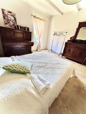 A bedroom with a large bed, a wooden dresser, a mirror, and a painting on the wall.