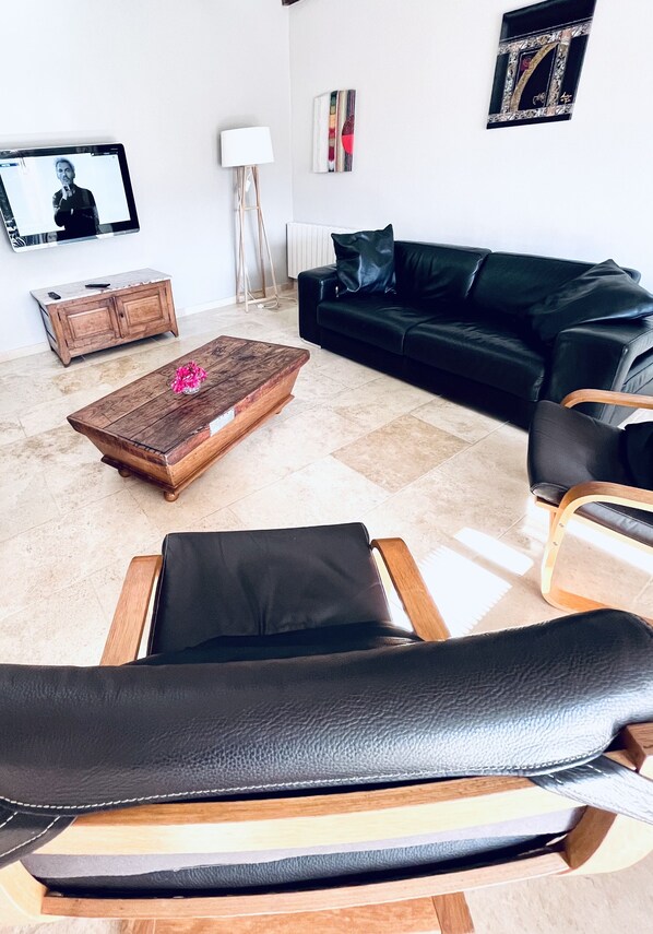 A modern living room with a black leather sofa, a wooden coffee table with a pink flower, a wooden cabinet, and a television on the wall.