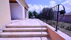 A set of stone steps leading to a covered outdoor area with a table and chairs, a metal railing, and a view of a residential area. - PROMOTION for May 26 MAY 1 JUNE (Saint-Florent)