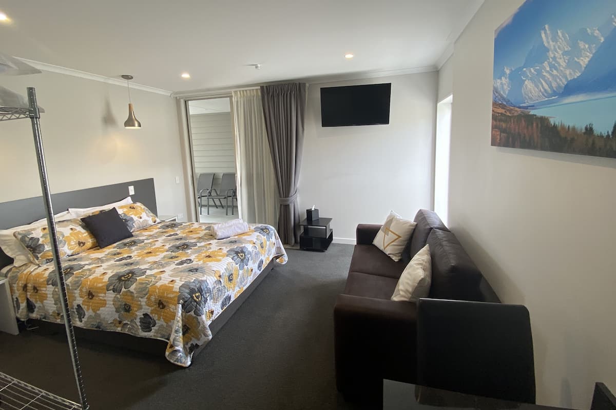 A hotel room with a bed, a sofa, a TV, and a painting of a mountain landscape.