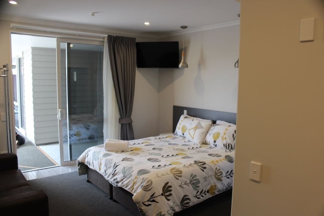 A bedroom with a bed, a TV mounted on the wall, and a sliding glass door leading to a balcony.