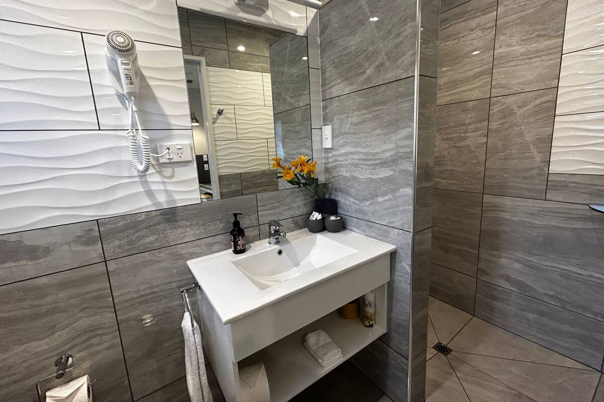 A modern bathroom with a white sink, dark tiles, and a handheld hair dryer.