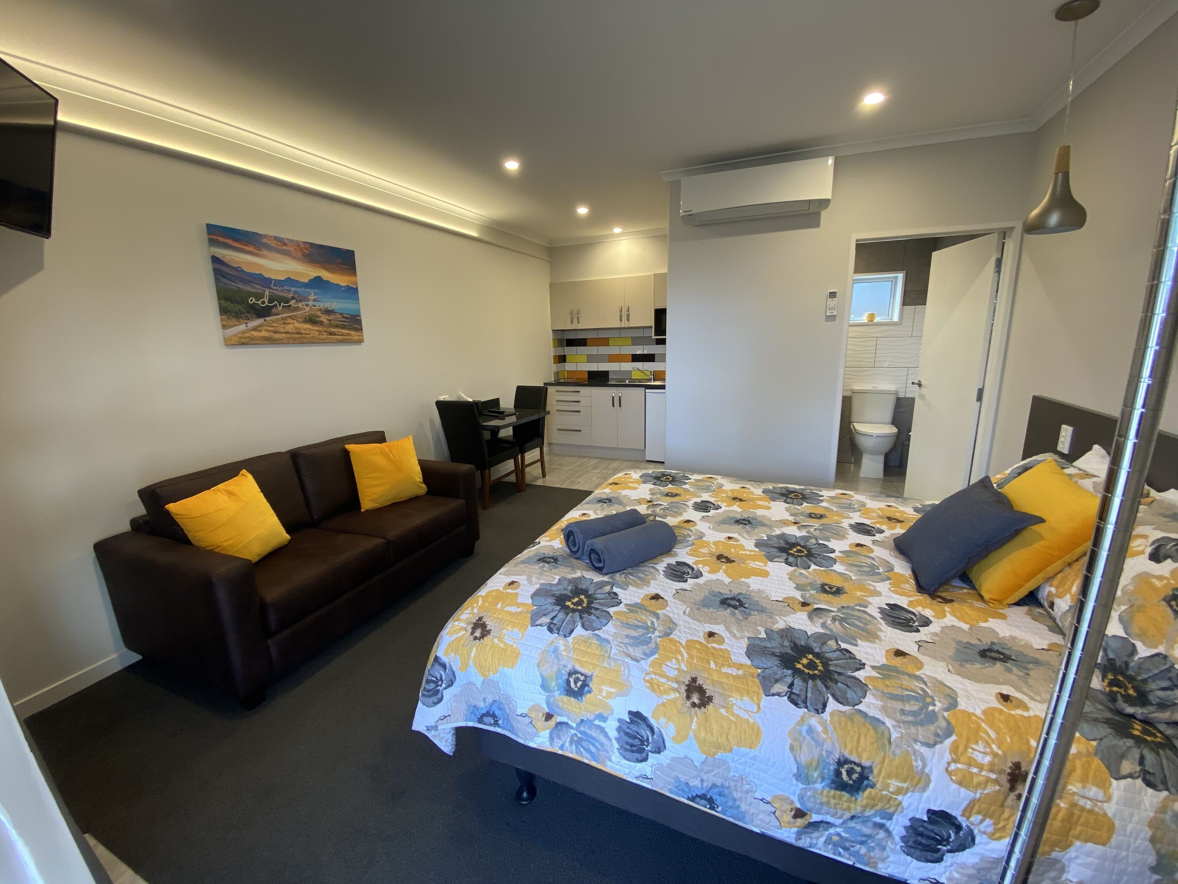 A modern bedroom with a large bed, a sofa, and a small kitchenette.