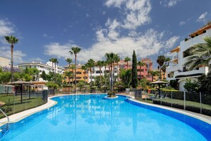 Une piscine entourée de palmiers et d’immeubles dotés de balcons.