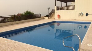 Ein Schwimmbecken mit Metallleiter, einer Fliesenveranda und einem überdachten Bereich mit Treppe.