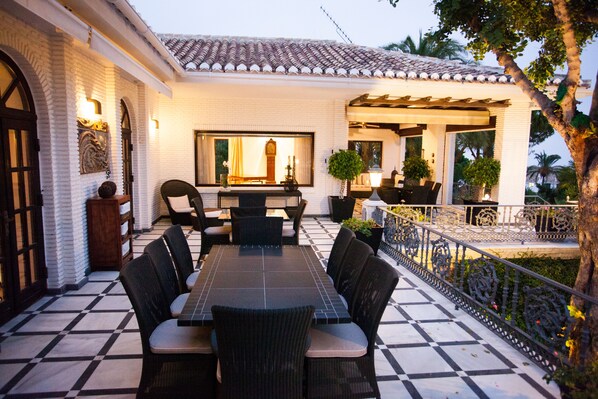 Une terrasse avec un sol carrelé, une table à manger avec des chaises et une pergola.