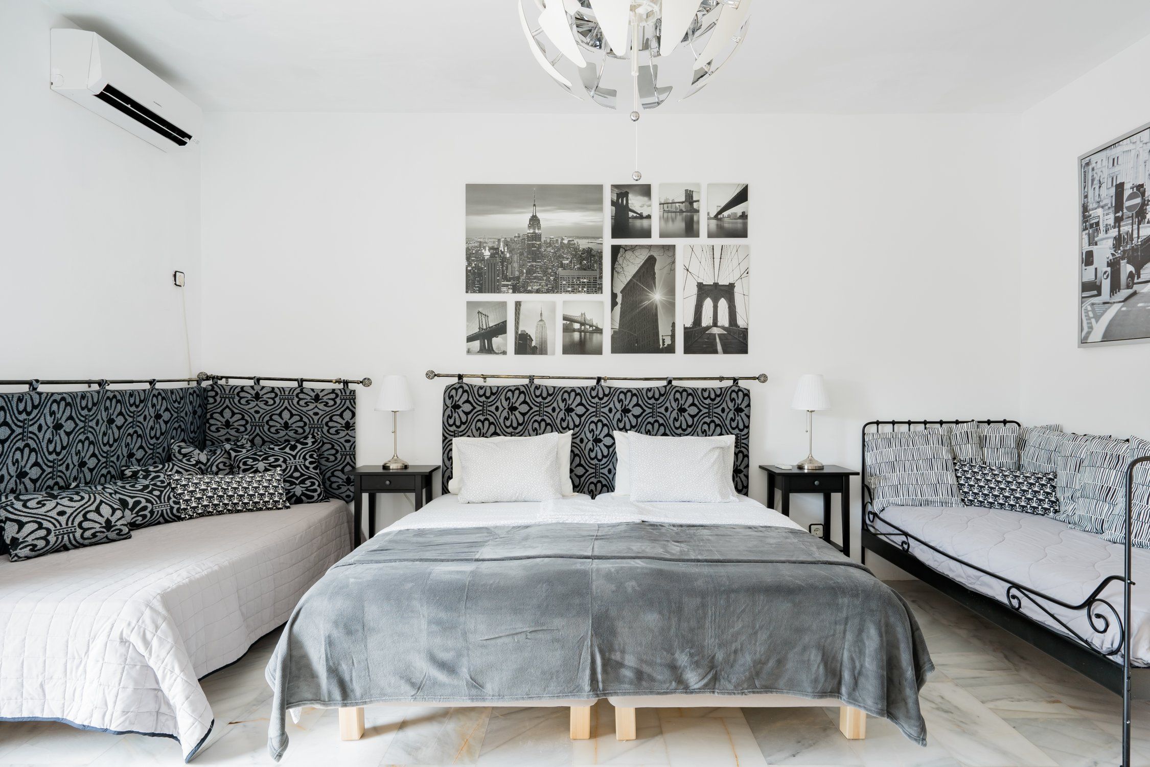 A bedroom with a large bed, two bedside tables, a wall-mounted air conditioner, and a cityscape photograph.