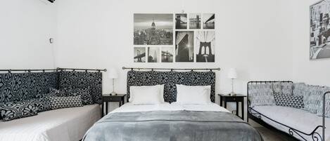 A bedroom with a large bed, two bedside tables, a wall-mounted air conditioner, and a cityscape photograph.