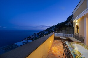 Una terraza con vistas al mar, una mesa con sillas y un edificio con balcón.