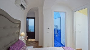 A bedroom with a large bed, a nightstand, and a lamp. There is a view of the sea through a window. - Golden Vaults, at few stairs from the road. It is easy to park in the area (Praiano)