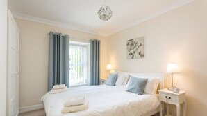 A neatly made bed with pillows and a bedside table with a lamp and clock. - Charming Original Stone Cottage Close To Beaches and Countryside (Alnwick)
