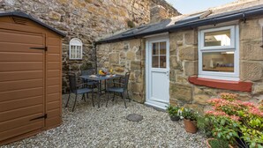 A stone building with a small patio area, a wooden door, and a window. - Charming Original Stone Cottage Close To Beaches and Countryside (Alnwick)