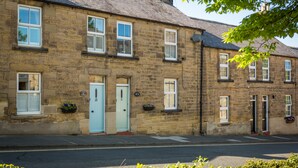 A stone building with multiple windows, a blue door, and a small garden area with flowers. - Charming Original Stone Cottage Close To Beaches and Countryside (Alnwick)