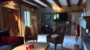 A cozy living area with a stone fireplace, two patterned armchairs, a wooden coffee table with red cups, and a television mounted on the wall. - CHALET LARGE COMFORT (Le Bouchet-Mont-Charvin)