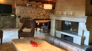 A cozy living room with a stone fireplace, a wooden ceiling, and a stone wall bookshelf. - CHALET LARGE COMFORT (Le Bouchet-Mont-Charvin)