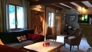 A cozy living room with a sofa, armchair, and a coffee table. There is a stone wall and a fireplace in the background. - CHALET LARGE COMFORT (Le Bouchet-Mont-Charvin)