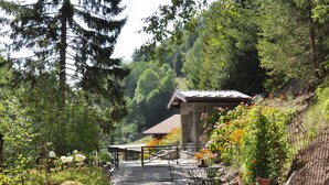A rustic outdoor seating area with a stone table and chairs, surrounded by greenery and a stone wall. - CHALET LARGE COMFORT (Le Bouchet-Mont-Charvin)