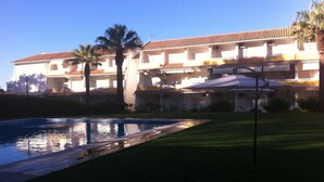 A hotel with a swimming pool, palm trees, and a tiled roof.