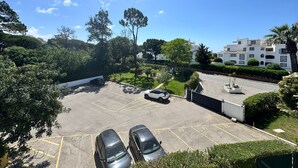A parking lot with two cars, surrounded by greenery and a building with multiple windows.