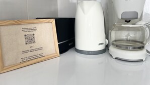 Una cafetera blanca, un objeto negro y un código QR enmarcado sobre una encimera.