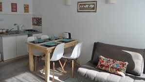 Un espacio habitable compacto con comedor, kitchenette y un sofá con un cojín colorido.