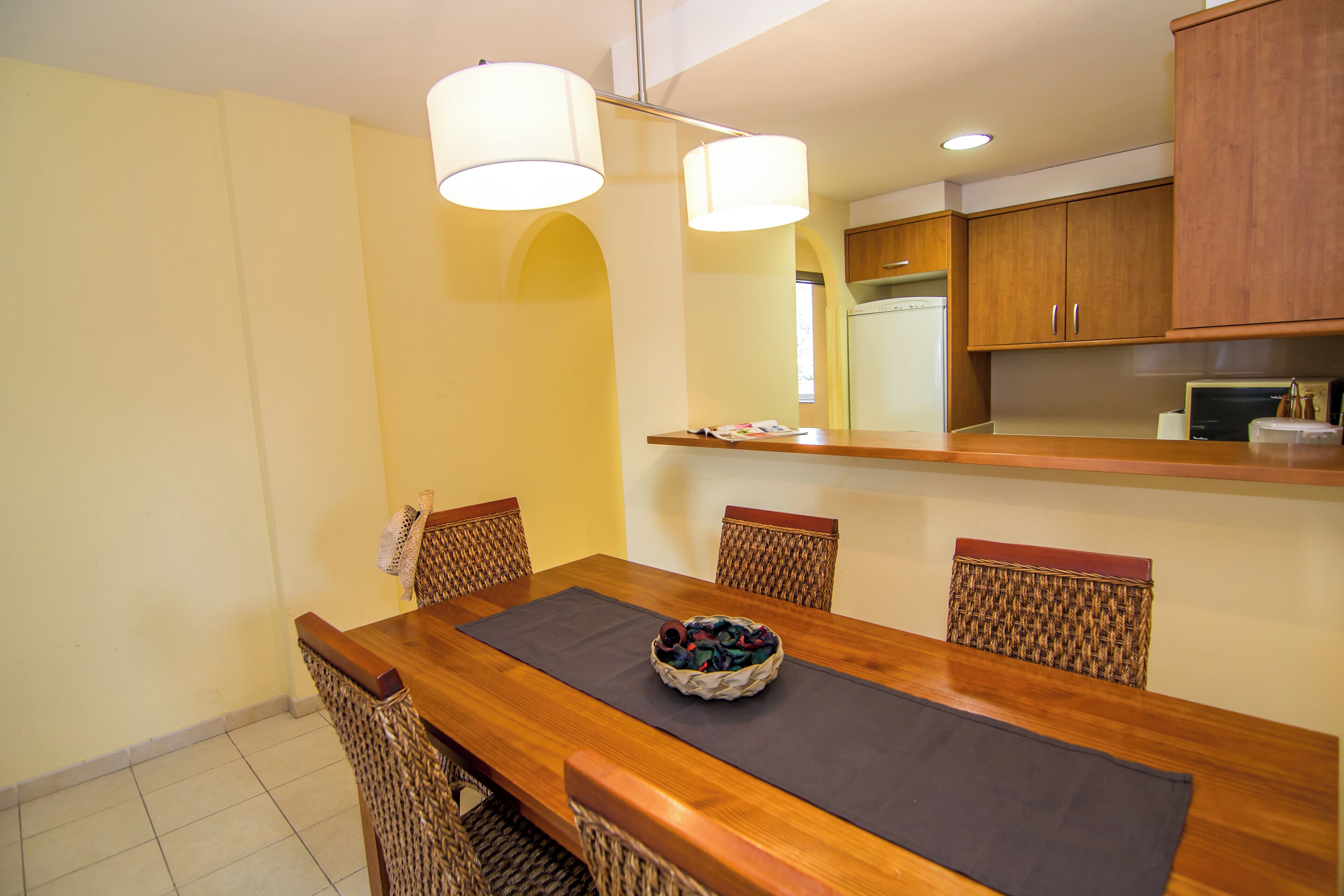 A dining area with a wooden table, four chairs, a bowl of fruit, and two pendant lights.