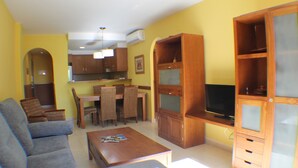 Un saló amb sofà, taula de centre, moble per a la televisió i zona de menjador amb cadires i taula.