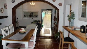 Zona pranzo con un lungo tavolo in legno, sedie bianche e un arco in mattoni.