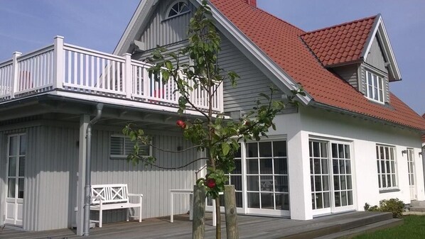Ein zweistöckiges Haus mit rotem Dach, weißer Fassade und einem Balkon mit weißen Geländern.