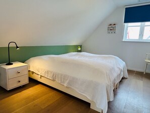 Ein Schlafzimmer mit einem Bett, einem Nachttisch, einer Lampe, einer grünen Wand, einem Fenster und einem kleinen Tisch.
