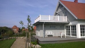 Ein zweistöckiges Haus mit einem Balkon, einer Holzterrasse und einem gepflasterten Weg, der zum Eingang führt.