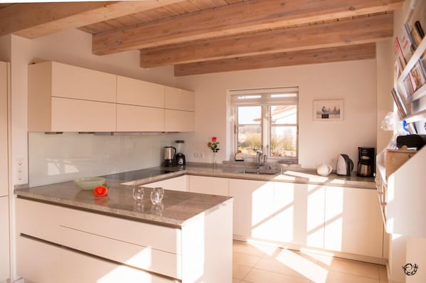A modern kitchen with white cabinets, a granite countertop, and a wooden ceiling. - Vacation home " Strand 22 ", on the Baltic Sea, roof terrace, sauna, WLAN by SEASIDE (Rosenhagen)
