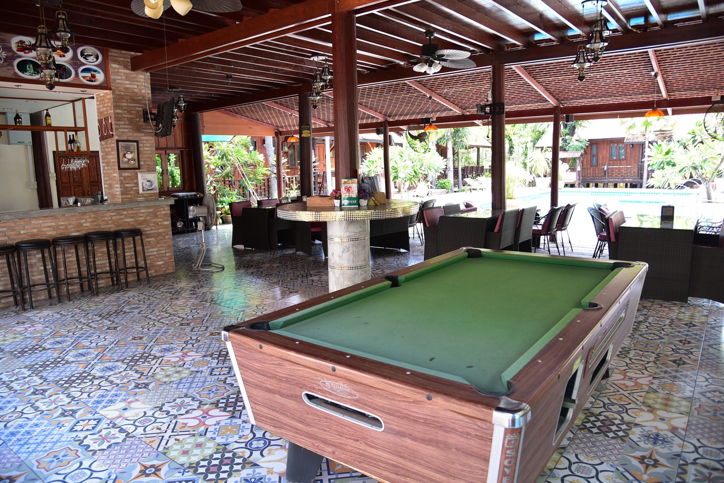 A pool table in a covered area with a tiled floor, a bar with stools, and outdoor seating.