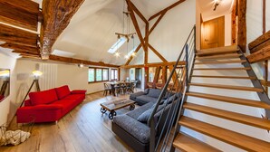 Ein geräumiger Dachboden mit freiliegenden Holzbalken, einem roten Sofa, einem grauen Ecksofa und einer Holztreppe.