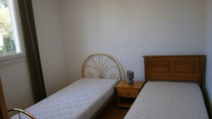 A small, simple room with two single beds, a nightstand, and a window with curtains. - semi-detached villa joint ownership of 7 villa located between st raphaél st tropez (Fréjus)