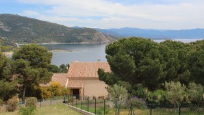 Una propietat a la costa amb jardí tancat, un edifici amb teulada i vista al mar i les muntanyes de fons.
