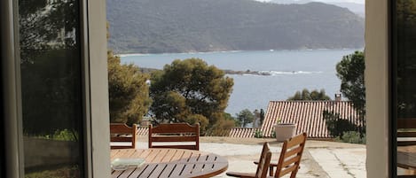 A patio with a table and chairs overlooking a coastal landscape with hills and a body of water.