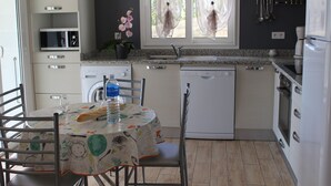 Una cuina amb taula de dinar preparada per a dues persones, rentadora i nevera.