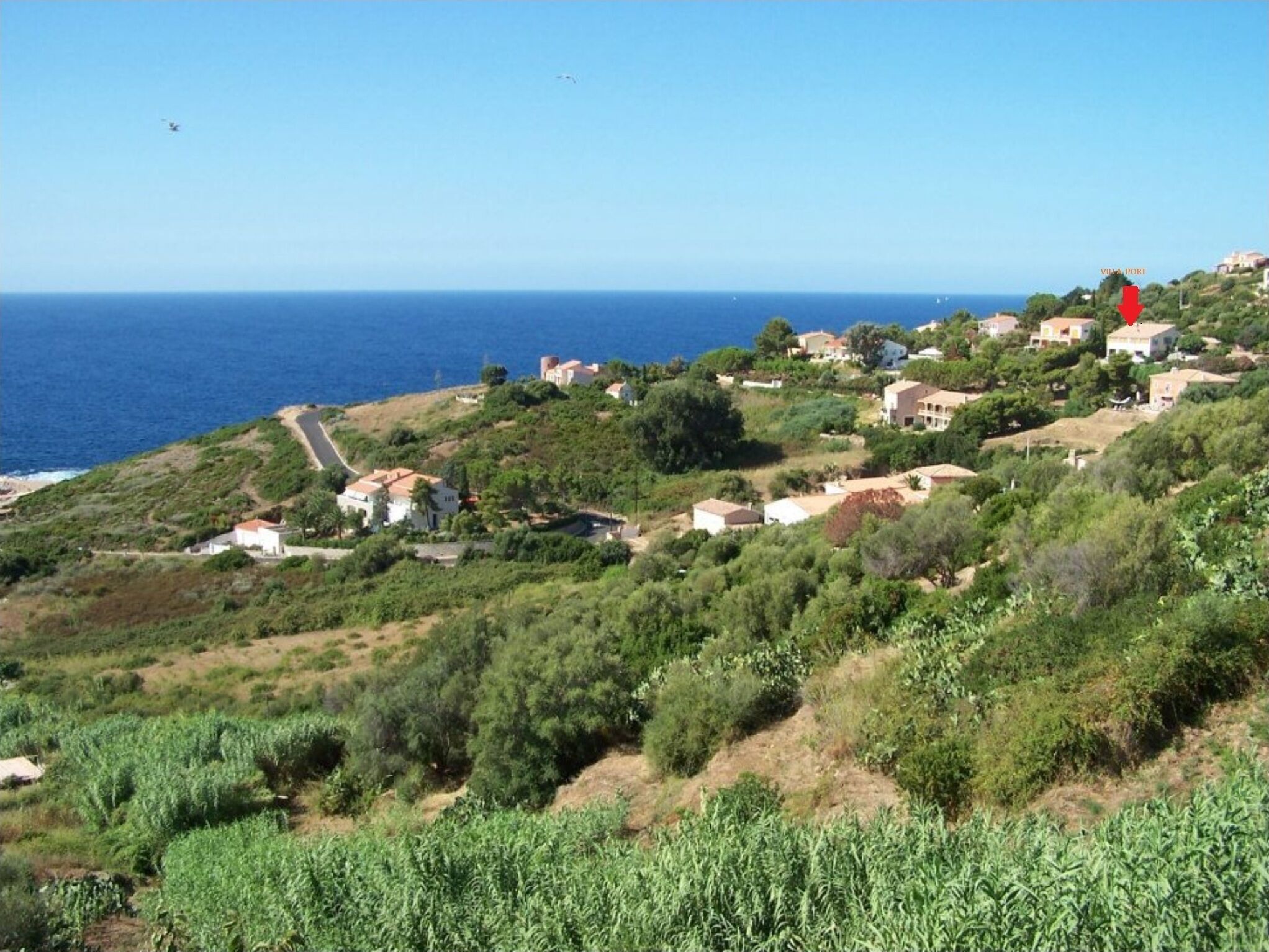 Ein Küstendorf mit Häusern an einem Hügel, einer Straße, die zum Strand hinunterführt, und freiem Blick auf das Meer.