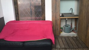 Una habitación pequeña y funcional con cama, microondas, lavamanos y ventana con mosquitero.