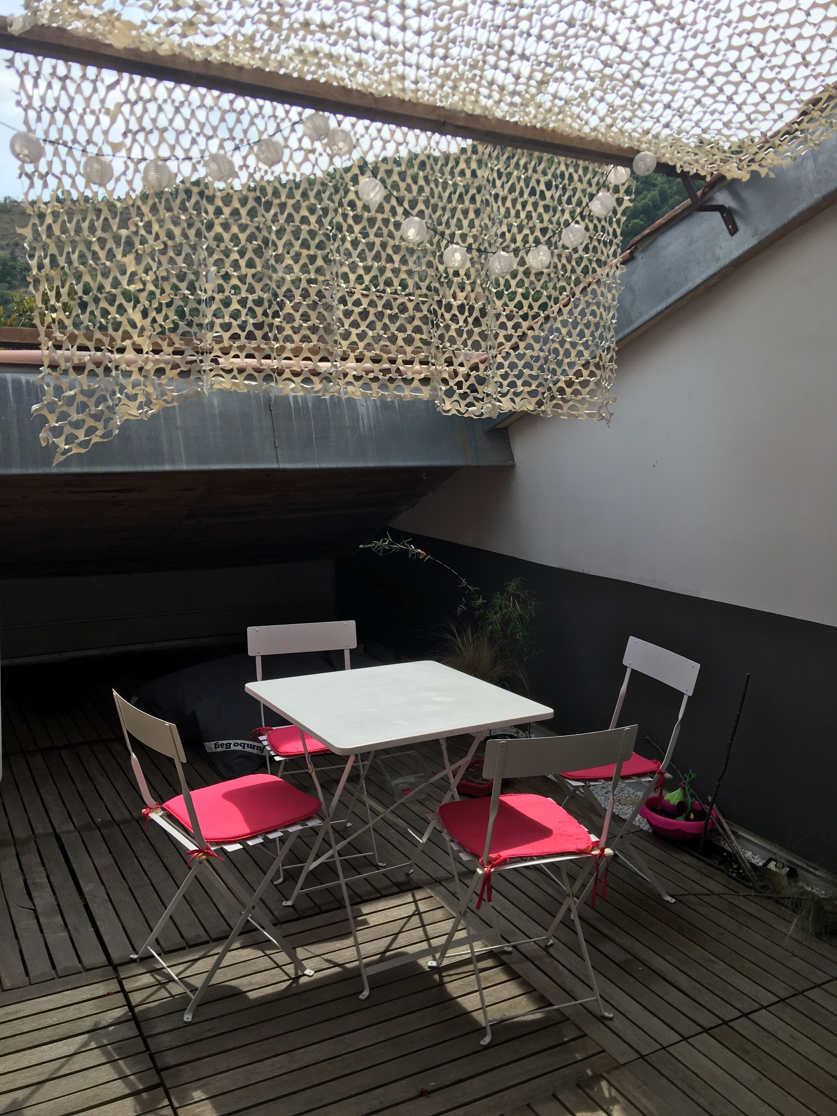 A covered outdoor seating area with a table and chairs, a decorative net, and a wooden wall.