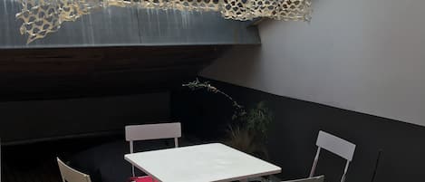 A covered outdoor seating area with a table and chairs, a decorative net, and a wooden wall.