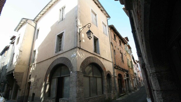 Una calle estrecha con edificios históricos, incluyendo un edificio con ventanas arqueadas y un letrero que indica un restaurante.