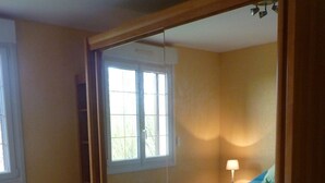 A bedroom with a large mirror, a bed with a blue bedspread, and a window with blinds.
