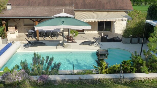 A backyard with a swimming pool, patio furniture, and a covered seating area.