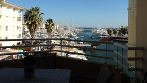 Een balkon met uitzicht op een jachthaven, palmbomen en gebouwen op de achtergrond.