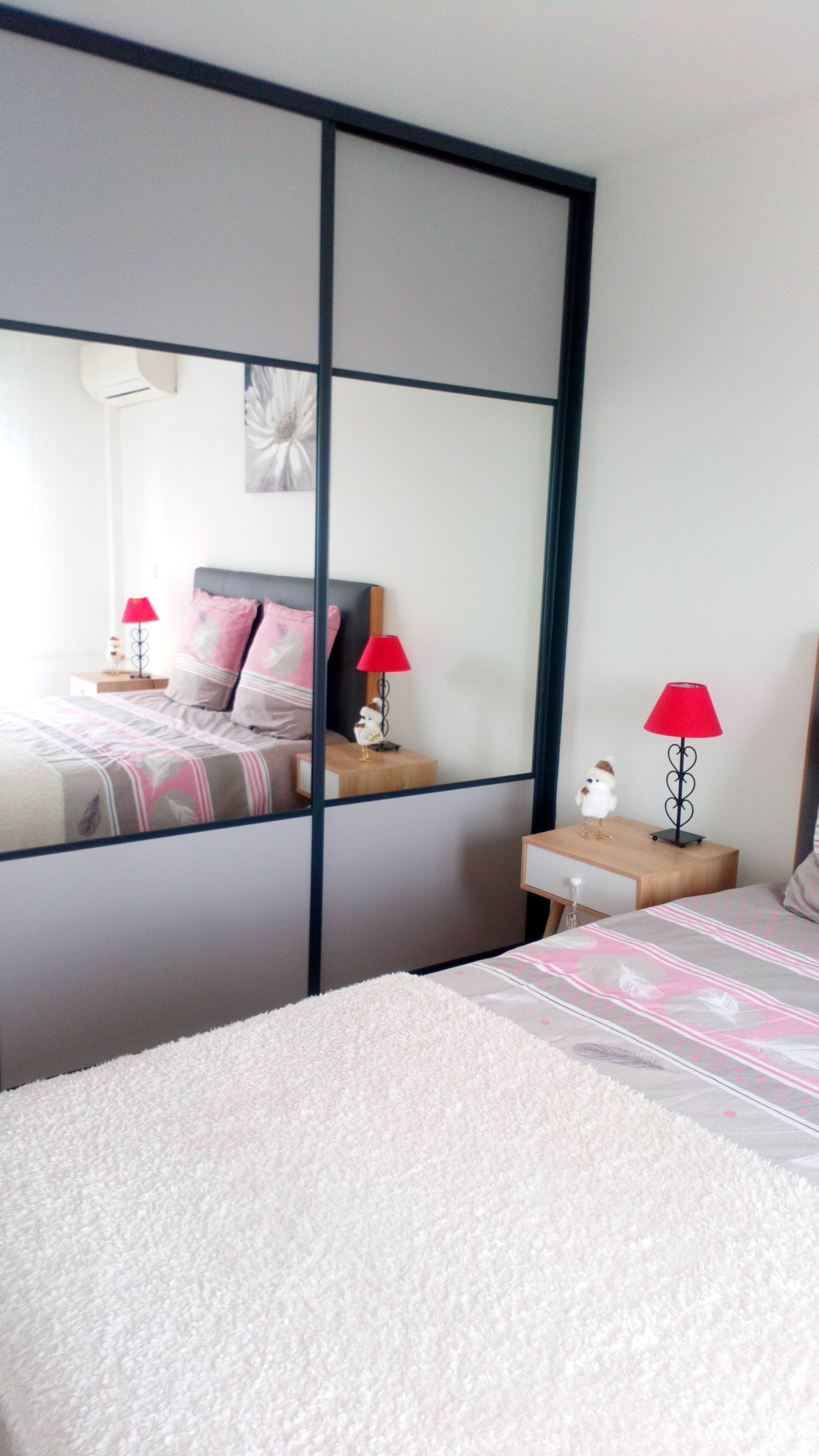 A bedroom with a bed, a nightstand, a mirror, and two red lamps.